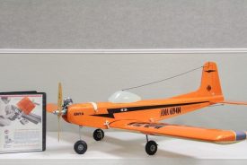 Orangefarbenes Fesselflugmodell Kwik-Fli Mk. II mit Enya-Motor, daneben ein Ordner mit der Original-Bauanleitung