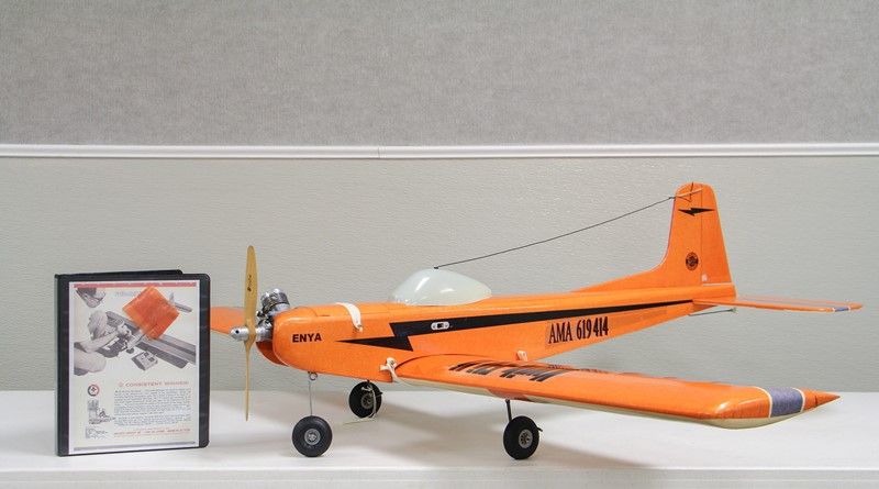 Orangefarbenes Fesselflugmodell Kwik-Fli Mk. II mit Enya-Motor, daneben ein Ordner mit der Original-Bauanleitung